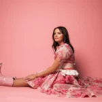 Abbie Callahan seated in a pink dress and boots against a pink background.