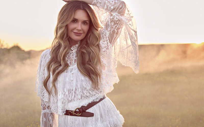 Carly Pearce posing outdoors in a white lace outfit.