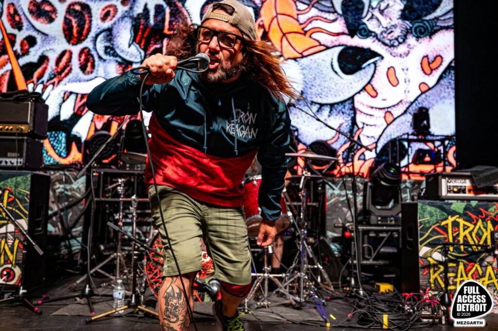 Iron Reagan singer holding a microphone in front of a colorful stage backdrop