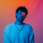 Austin Snell portrait lit in blue against an orange and purple background