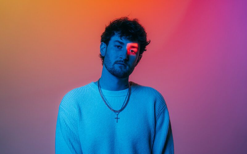 Austin Snell portrait lit in blue against an orange and purple background