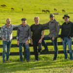 The members of Exile standing beside a fence in a green field