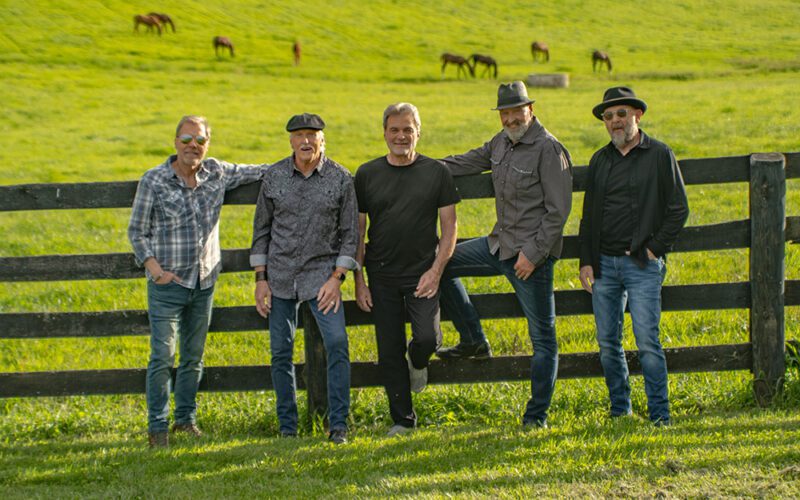 The members of Exile standing beside a fence in a green field