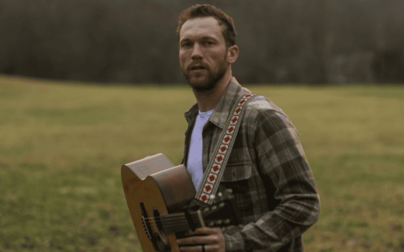 Phillip Phillips carrying a guitar in a grassy field