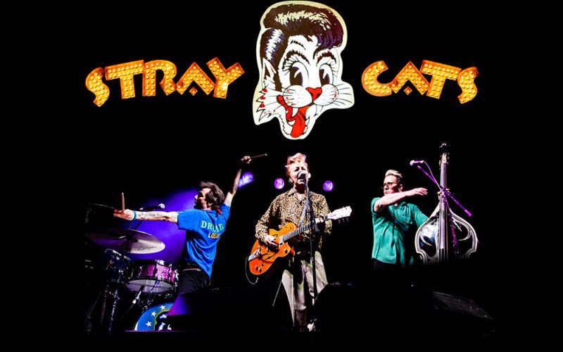 Stray Cats performing on stage beneath the band's logo