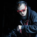 Slipknot's Sid Wilson wearing sunglasses against a dark background
